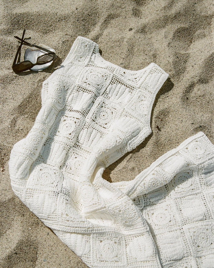 Off-model view of the LSPACE Calla Dress in cream, laid flat on sand to show the sleeveless crochet silhouette with granny-square motif detailing.