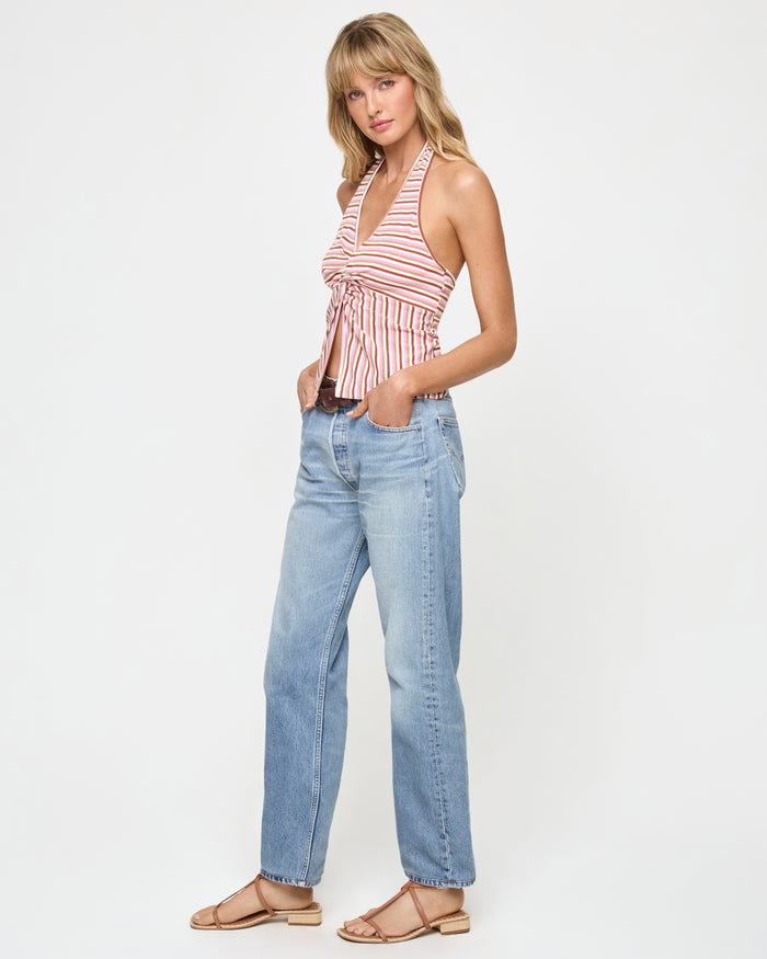 Three-quarter view of a model wearing the LSPACE Callie Halter in azalea stripe, showing the ruched center-front detail of the ribbed stripe halter top, styled with light-wash jeans.