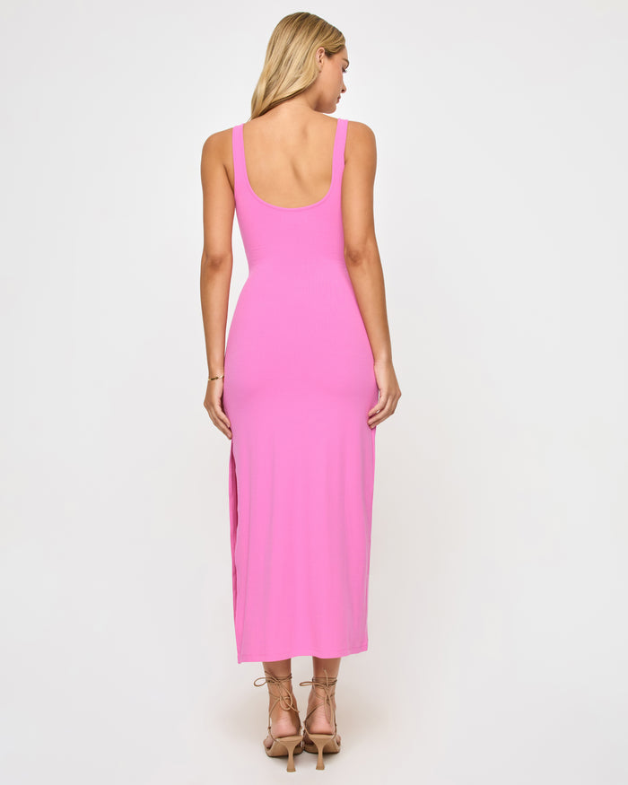 Back view of a model wearing the LSPACE Camille Dress in hottest pink, showing the low scoop back with thick tank straps and side slit of the bright pink midi dress.