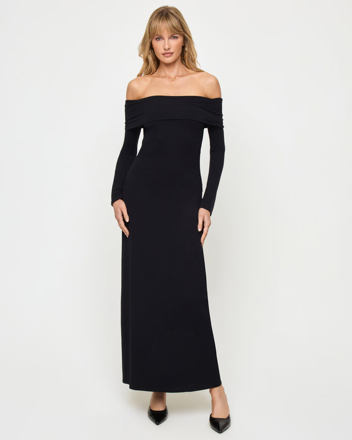 Front view of a model wearing the LSPACE Carrie Dress in black, featuring an off-the-shoulder neckline with a folded band, long sleeves, and a body-hugging maxi silhouette in ribbed black knit fabric.