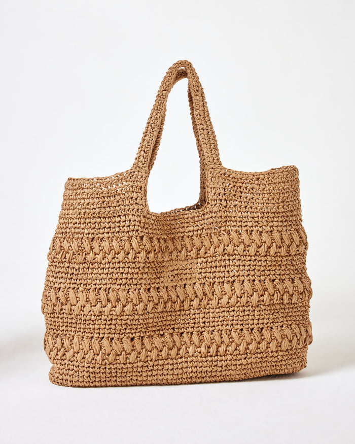 Side view of the Changing Tides Bag in natural, a large crochet raffia tote, on a white background.