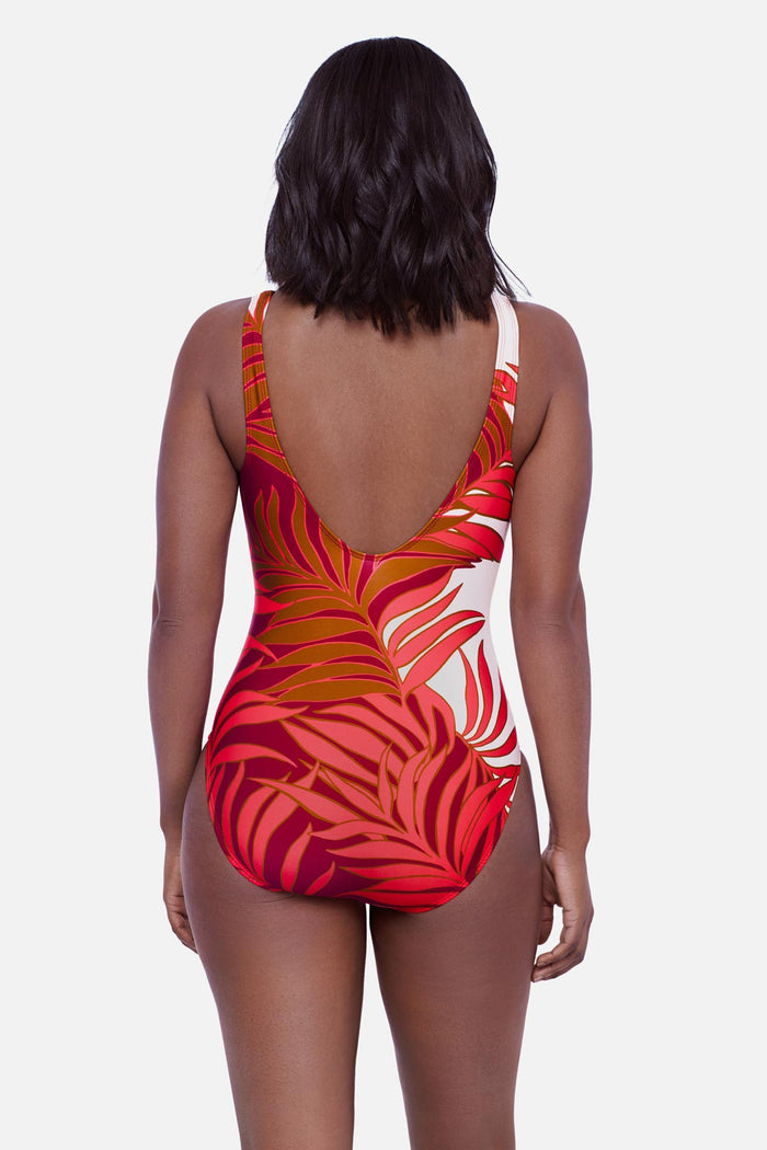 Woman turned away wearing an orange and white palm leaf printed one-piece swimsuit