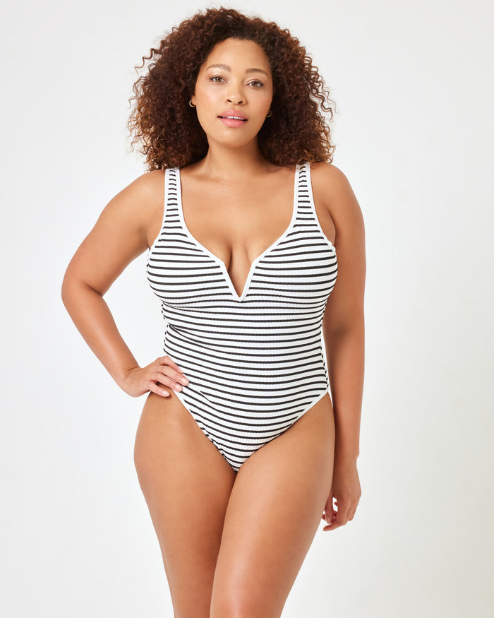 Front view of a model wearing the LSPACE Sail Along Stripe Coco One Piece Swimsuit, featuring a plunging V-neckline and navy and white horizontal stripes.