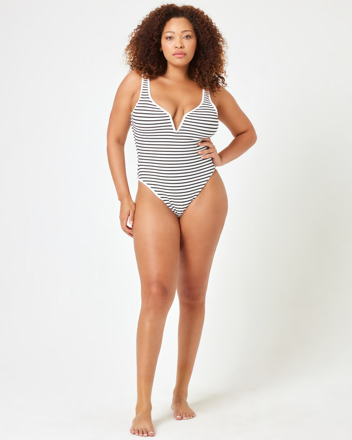 Full-length front view of a model wearing the LSPACE Sail Along Stripe Coco One Piece Swimsuit, showcasing the plunging V-neckline and high-cut leg of the navy and white striped one-piece.