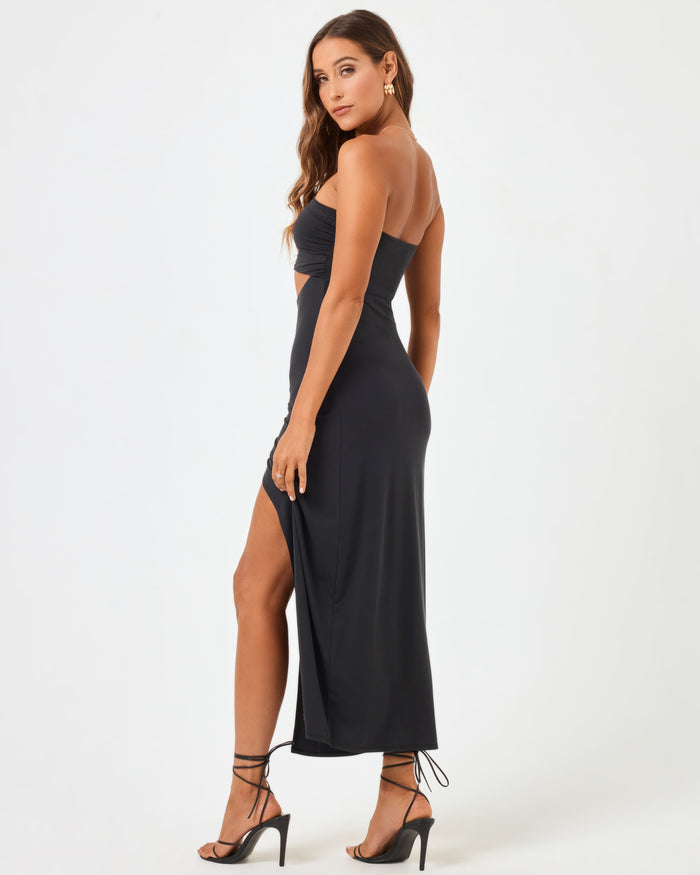 Back angled view of a model wearing the LSPACE Corsica Dress in black, showing the side slit.