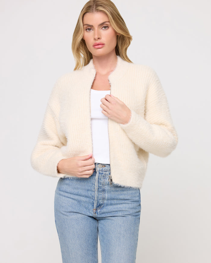 Close-up front view of a model wearing the LSPACE Cosmos Sweater in tapioca, an open-front fuzzy sweater in a warm cream color, layered over a white tank.