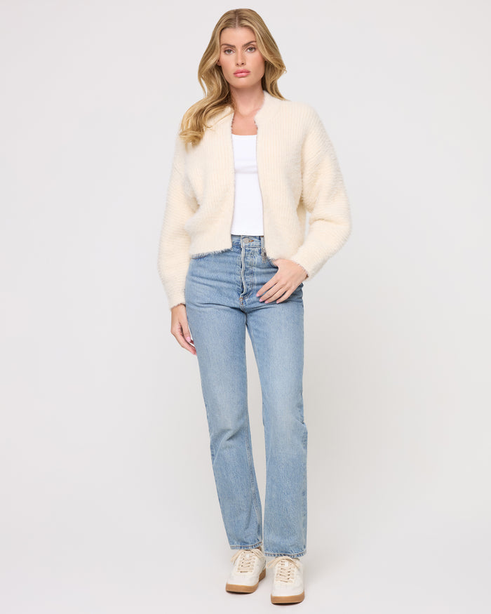 Front view of a model wearing the LSPACE Cosmos Sweater in tapioca, a cropped open-front fuzzy sweater in cream, styled with jeans and sneakers.