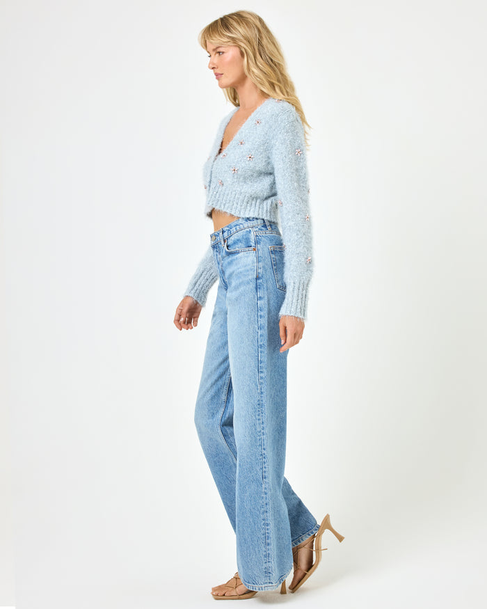 Full body side view of a model wearing the LSPACE Crystal Cardigan in dove, showing the cropped silhouette and long sleeves of the fluffy knit cardigan with crystal floral embellishments, styled with wide-leg jeans.