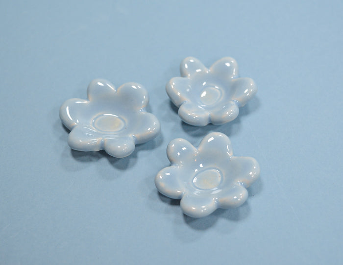 Three small glossy white flower-shaped dish holders arranged on a light blue background.