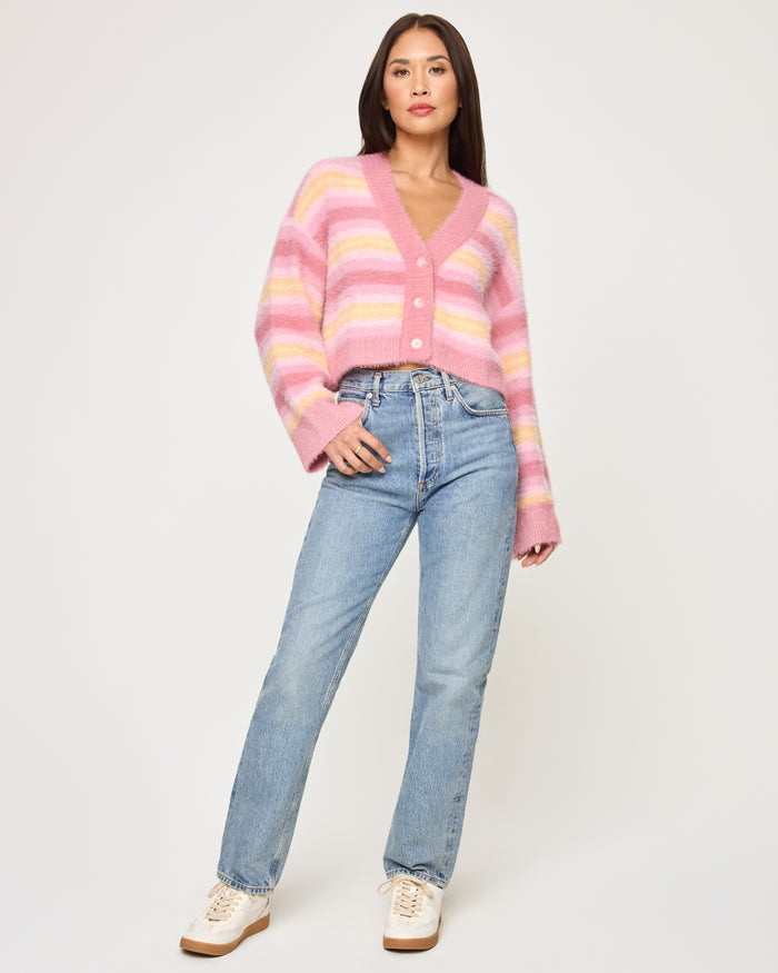 Full-length front view of a model wearing the LSPACE Daybreak Cardigan in daybreak stripe, a cropped fuzzy cardigan with pink and yellow pastel stripes, V-neckline, and button front.