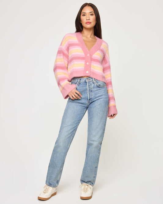 Full-length front view of a model wearing the LSPACE Daybreak Cardigan in daybreak stripe, a cropped fuzzy cardigan with pink and yellow pastel stripes, V-neckline, and button front.