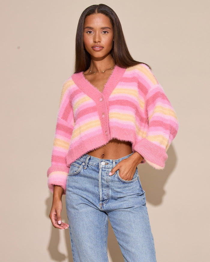 Front view of a model wearing the LSPACE Daybreak Cardigan in daybreak stripe, an open cropped fuzzy cardigan in pink and yellow pastel stripe, styled with jeans.