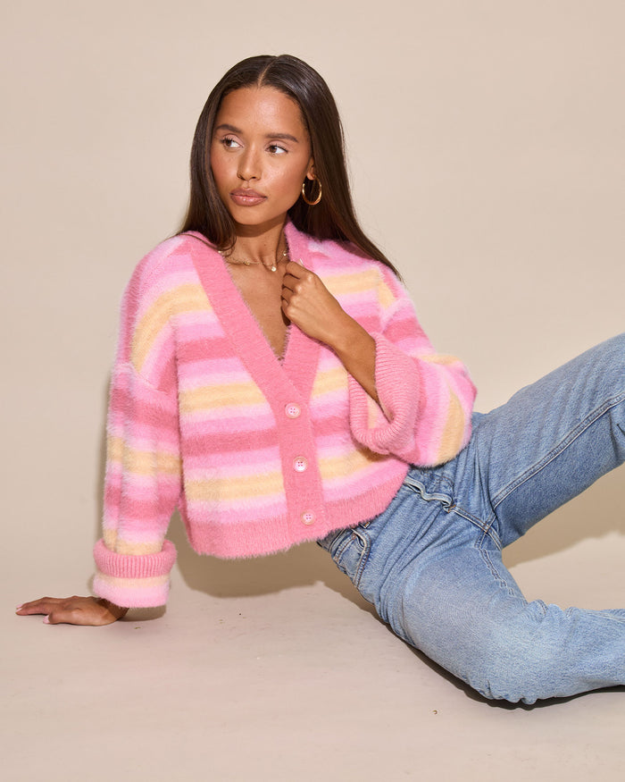 Editorial seated pose of a model wearing the LSPACE Daybreak Cardigan in daybreak stripe, shown in a warm-toned studio setting.