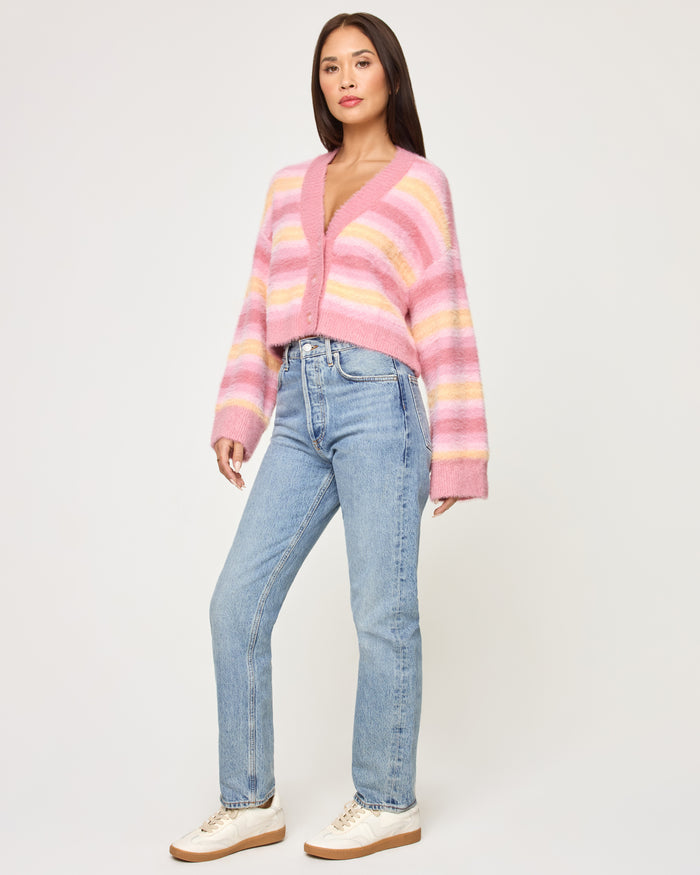 Three-quarter front view of a model wearing the LSPACE Daybreak Cardigan in daybreak stripe, showing the pastel pink and yellow stripe pattern.