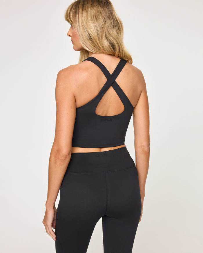 Back view of model wearing the Declan Top in black showing the crossback strap detail with cutout, with black flare legging.