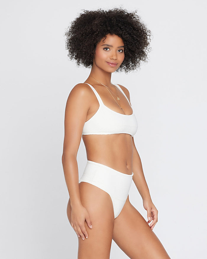Side view of a model wearing the LSPACE cream Desi Bikini Bottom, a ribbed high-waist style, paired with the cream Jess Bikini Top.
