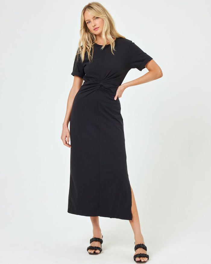 Front view of a model wearing the LSPACE Drew Dress in black, a short-sleeve jersey midi dress with a twisted knot at the waist and side slit.