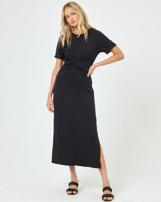 Front view of a model wearing the LSPACE Drew Dress in black, a short-sleeve jersey midi dress with a twisted knot at the waist and side slit.