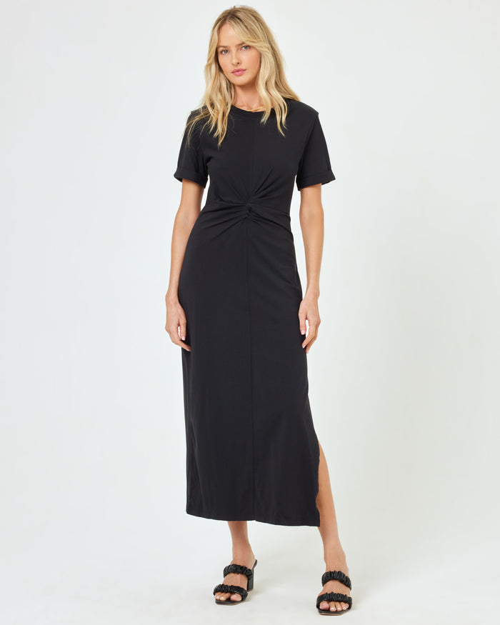 Full body front view of a model wearing the LSPACE Drew Dress in black, a short-sleeve jersey midi dress with a twisted knot detail at the waist.