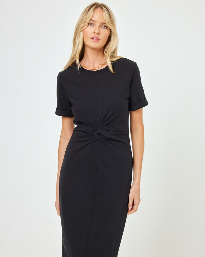 Close-up front view from mid-torso of a model wearing the LSPACE Drew Dress in black, highlighting the twisted knot waist detail.