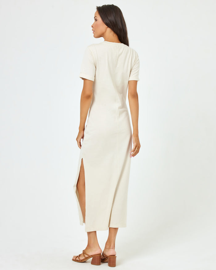 Back view of a model wearing the LSPACE Drew Dress in cream, a short-sleeve jersey midi dress with a side slit.
