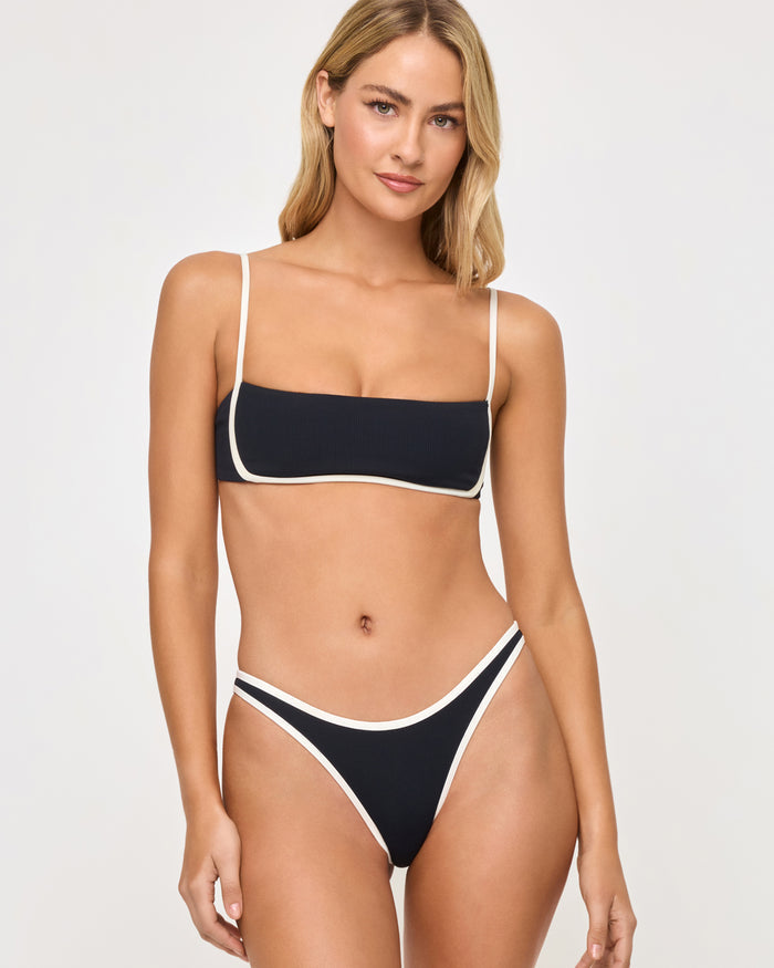 Front view of a model wearing the LSPACE black-cream Elle Bikini Bottom, a high-cut cheeky style with cream piping trim, paired with a matching black-cream Hazel Bikini Top.