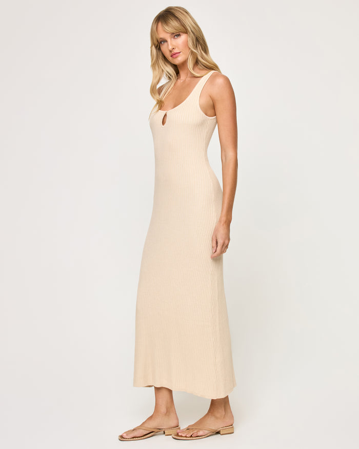 Side view of a model wearing the LSPACE En Route Dress - Oat in oat, showing the ribbed knit texture and slightly flared hem of the sleeveless maxi dress.