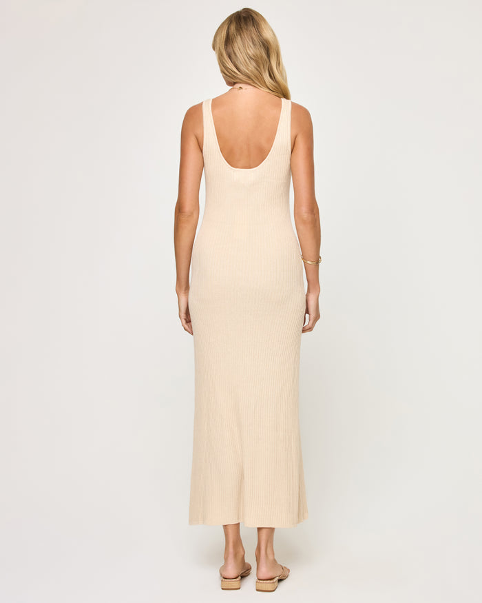 Back view of a model wearing the LSPACE En Route Dress - Oat in oat, showing the scoop back neckline and wide straps of the ribbed knit sleeveless maxi dress.
