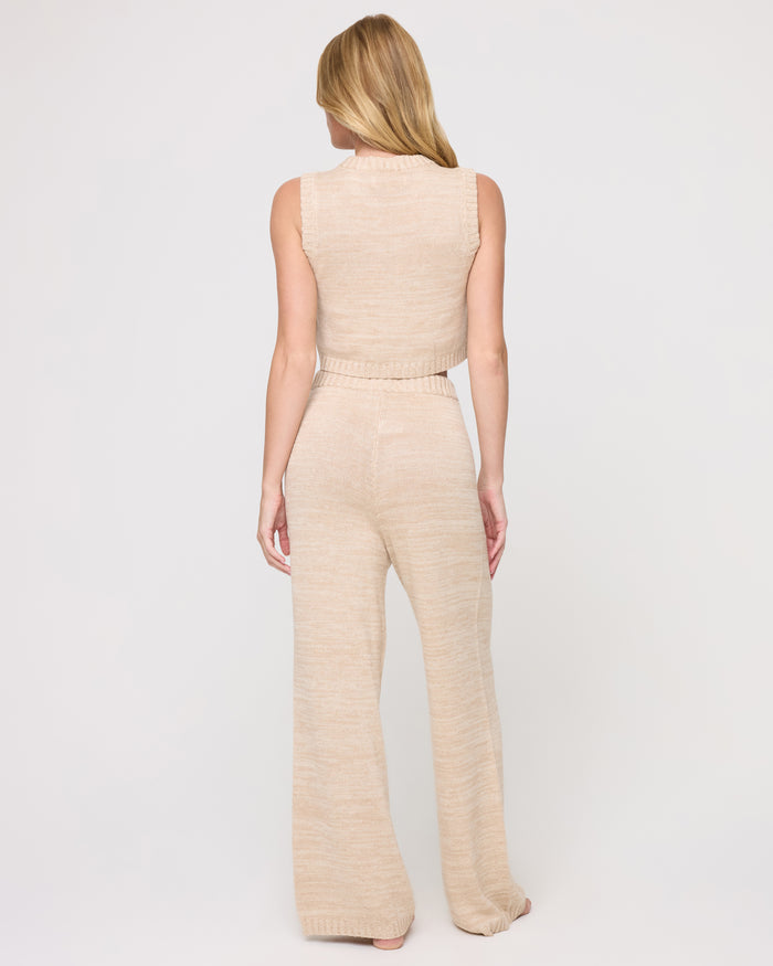 Back view of a model wearing the LSPACE En Route Pant - Heather Oatmeal in heather oatmeal, showing the elastic waistband and wide-leg flare of the knit pant.