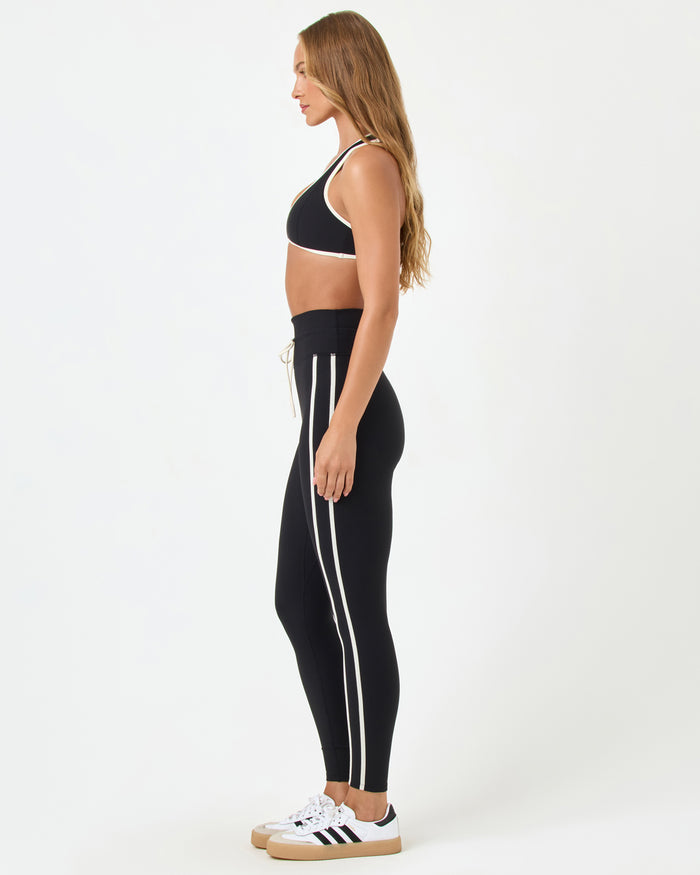 Side view of the LSPACE Finley Bra in black-cream on a model against a white background, paired with black high-rise active pants with cream trim, showing the profile silhouette.
