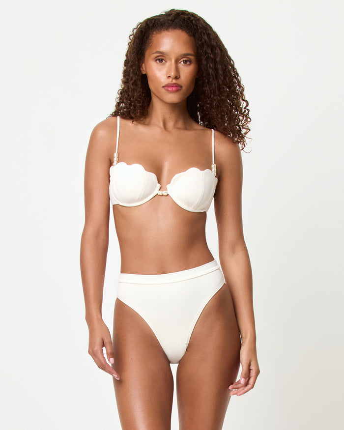 Front view of a model in a studio wearing the LSPACE cream Sunrise Shell Bikini Top with scalloped shell-edged cups and pearl center embellishment, paired with Frenchi Bikini Bottom.