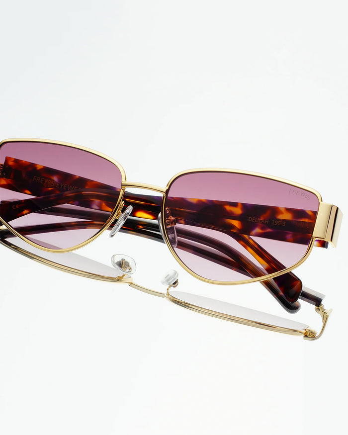 Close-up detail of the Freyrs Delilah Sunglasses in gold showing the gold metal frame, tortoise arms, and pink lenses.
