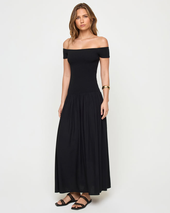 Three-quarter front view of a model wearing the LSPACE Going Steady Midi in black, showing the full silhouette of the off-the-shoulder midi dress with fitted ribbed bodice and gathered skirt.