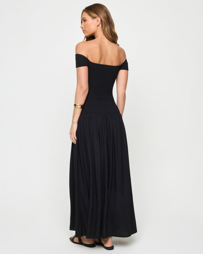 Back view of a model wearing the LSPACE Going Steady Midi in black, showing the open low scoop back of the off-the-shoulder dress and gathered full skirt.