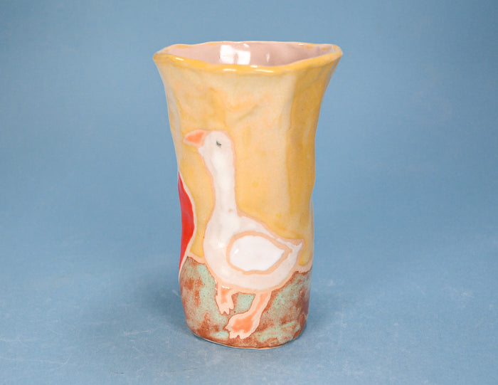 A handmade ceramic vase featuring a painted white goose on a textured yellow and orange body, set against a solid blue background.
