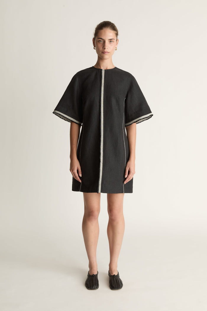 Black dress with white trim worn by a model on a light background