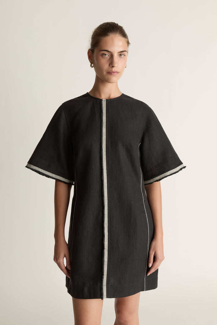 Black dress with white trim worn by a model on a light background