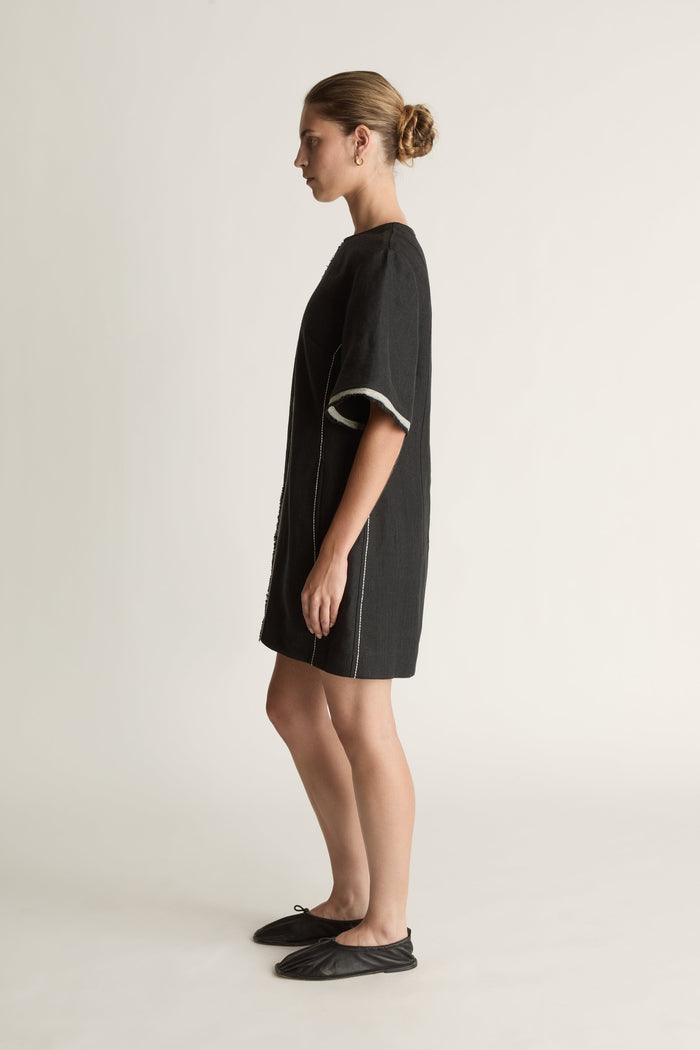 Black dress with white trim worn by a model on a light background