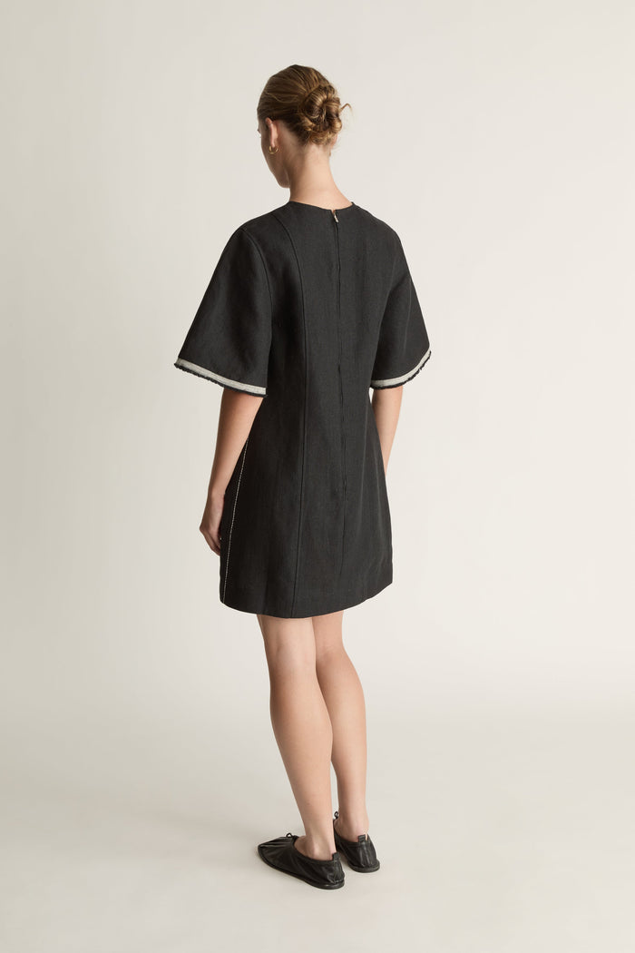 Black dress with white trim worn by a model on a light background