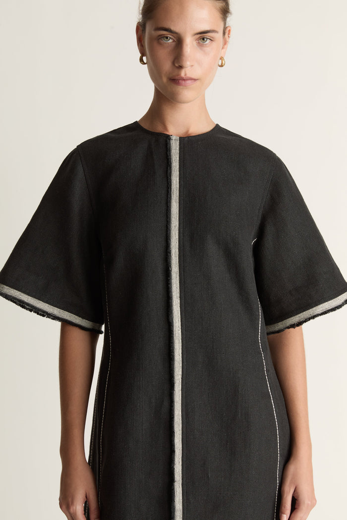 Black dress with white trim worn by a model on a light background
