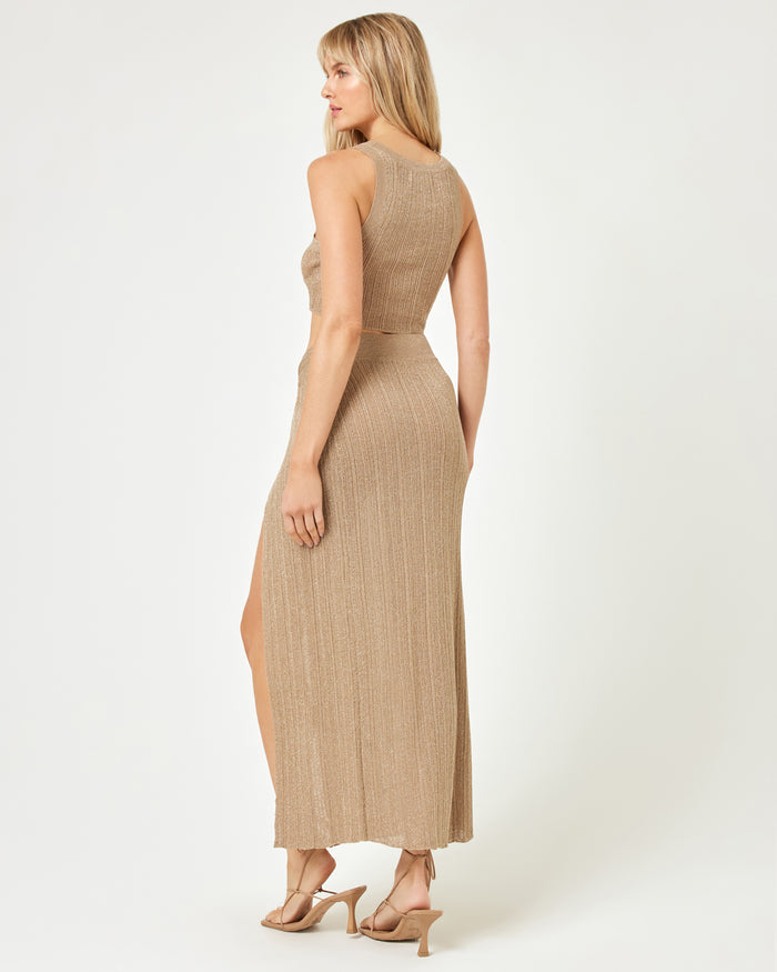 Back view of a model wearing the LSPACE Heart Of Gold Tank in metallic gold, paired with the matching maxi skirt, showing the open back and racerback-style construction of the ribbed metallic knit crop top.