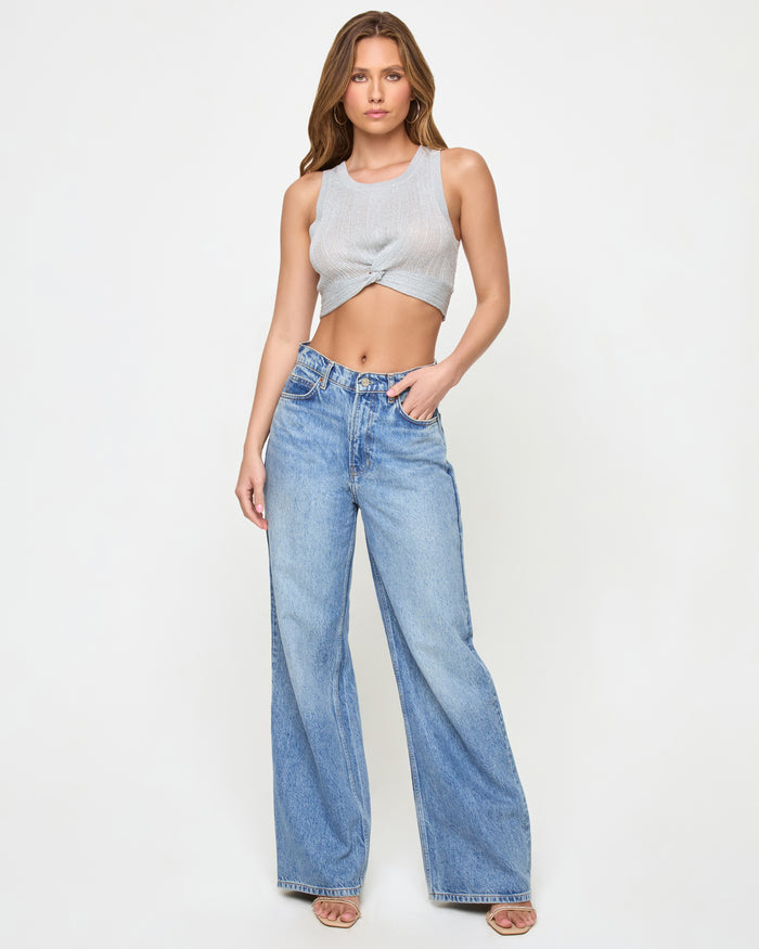 Front view of a model wearing the LSPACE Heart Of Gold Tank in metallic silver, a cropped twisted-front tank styled with wide-leg denim jeans.