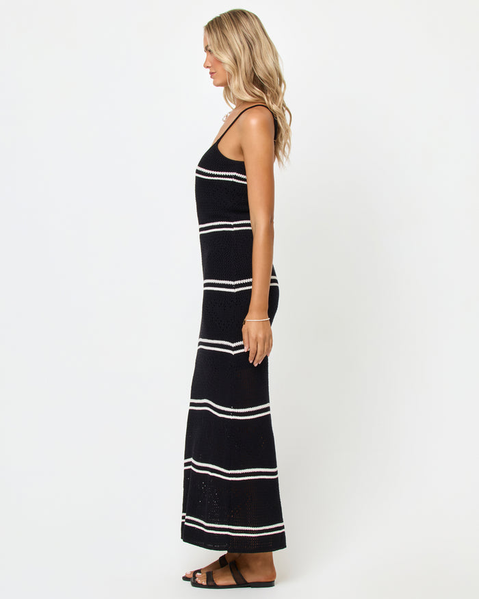 Side view of a model wearing the LSPACE Heart To Heart Dress in black-cream, showing the profile with the body-hugging crochet maxi silhouette in black with horizontal cream stripes and spaghetti straps.