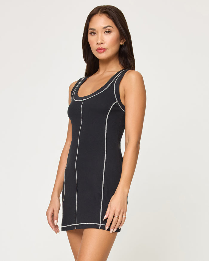 Three-quarter front view of a model wearing the LSPACE Highline Dress - Black in black, showing the side silhouette and white contrast topstitching of the sleeveless mini dress.