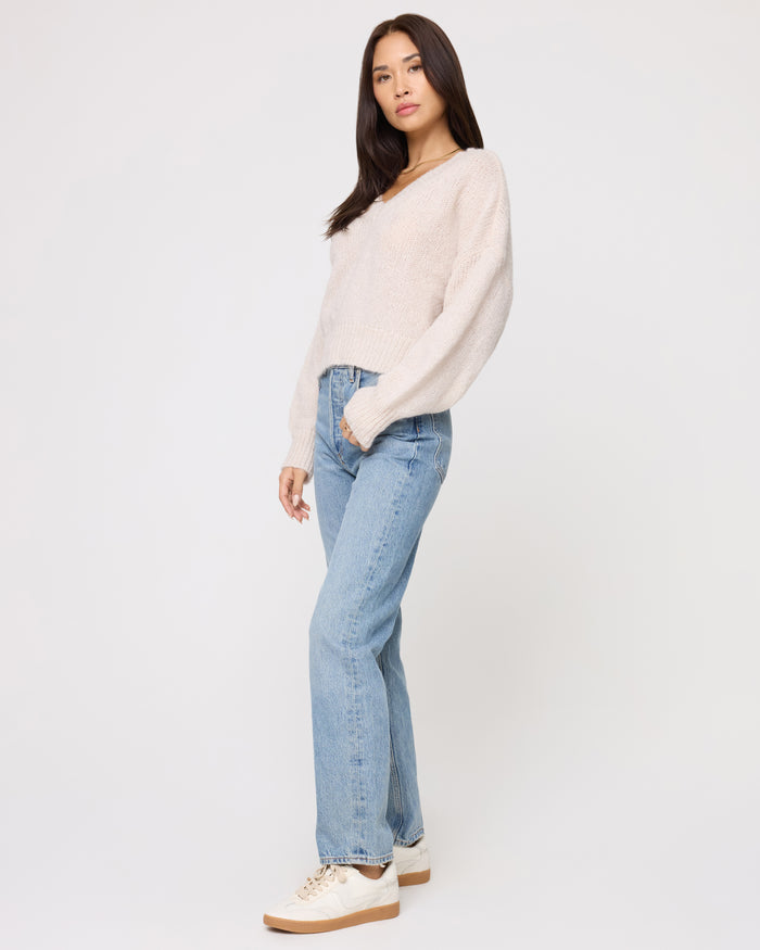 Side view of a model wearing the LSPACE Icon Pullover - Oat in oat, showing the oversized silhouette and long sleeves of the knit pullover, styled with light wash jeans.