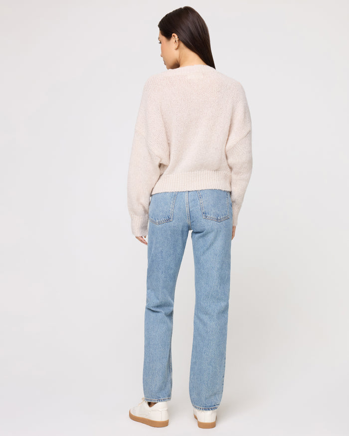 Back view of a model wearing the LSPACE Icon Pullover - Oat in oat, showing the back of the oversized knit pullover and ribbed hem, styled with light wash jeans.