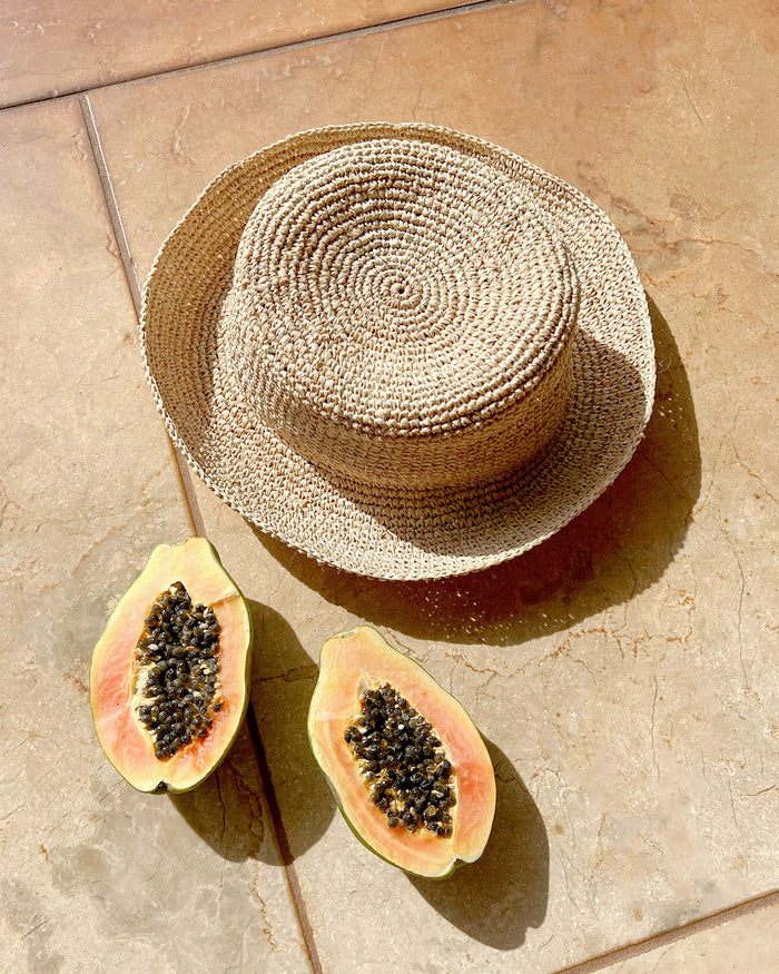 Flat lay of the Isadora Bucket Hat in natural styled with tropical fruits on a terracotta tile.
