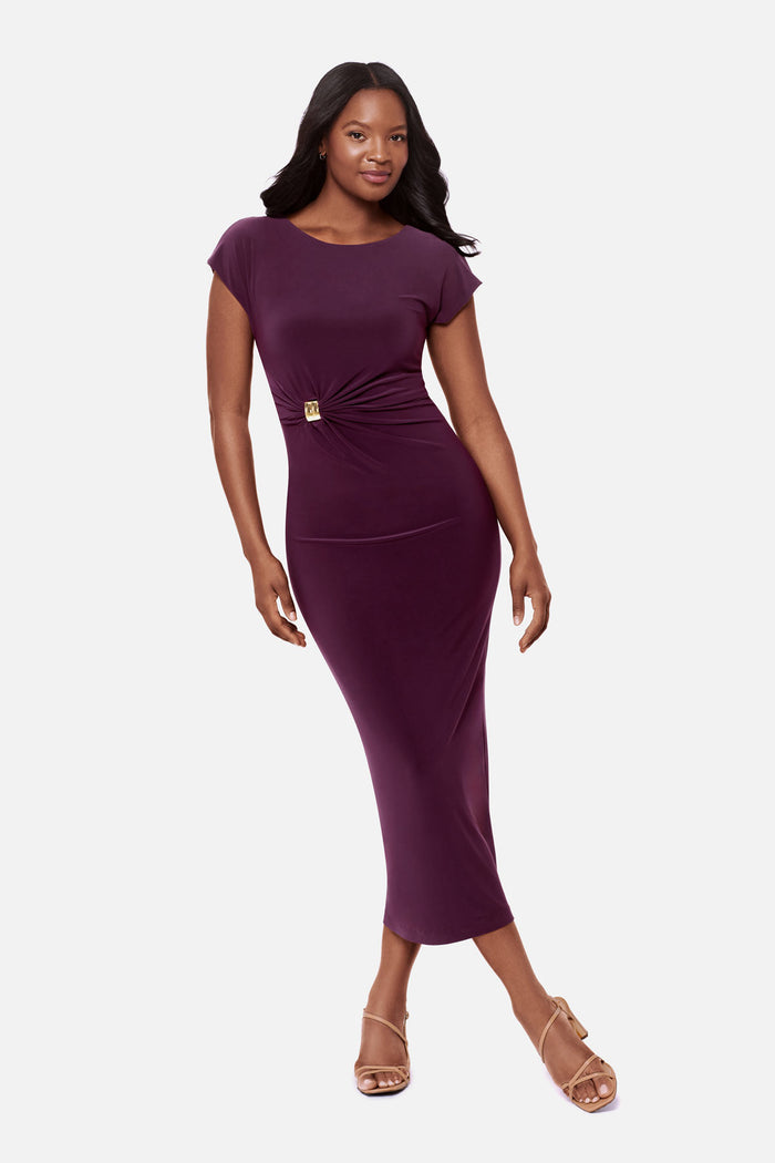 Woman wearing a dark purple short sleeve dress with a gold tone hardware detail on the side