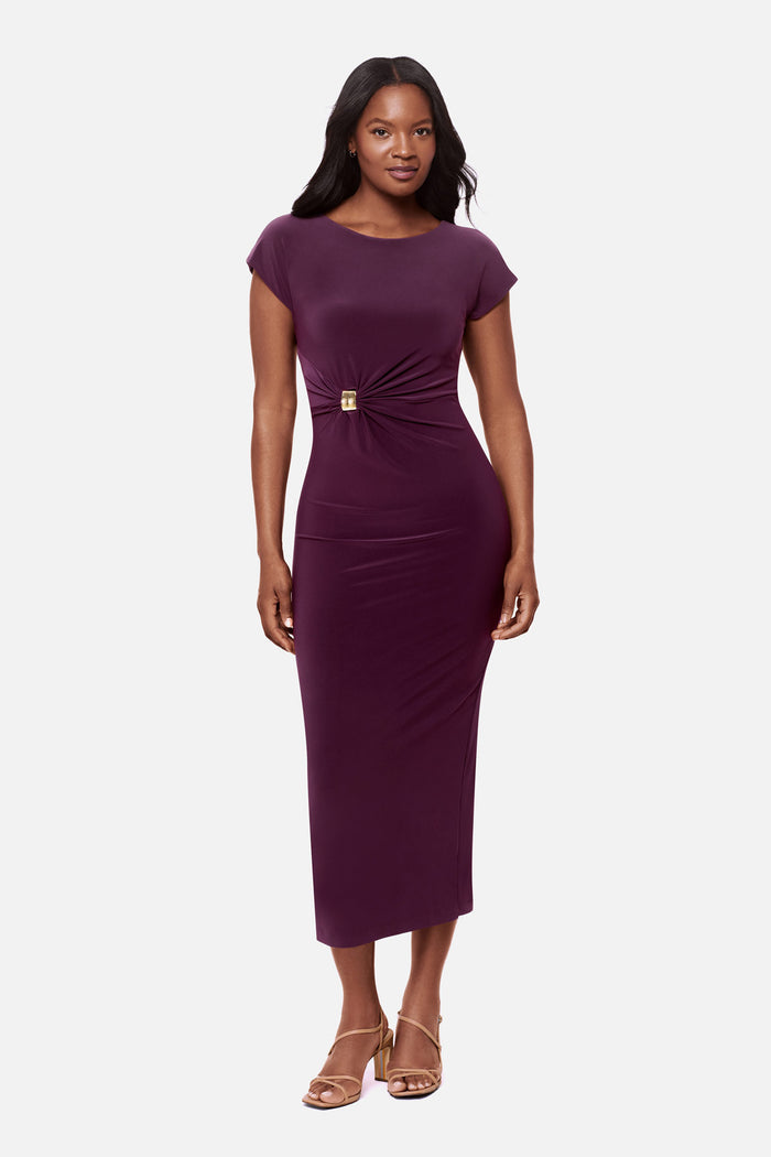 Woman wearing a dark purple short sleeve dress with a gold tone hardware detail on the side