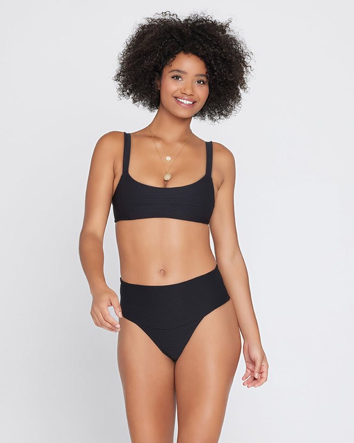 Front view of a model wearing the LSPACE black Jess Bikini Top, a ribbed bralette style with a square neckline, paired with the black Desi Bikini Bottom.